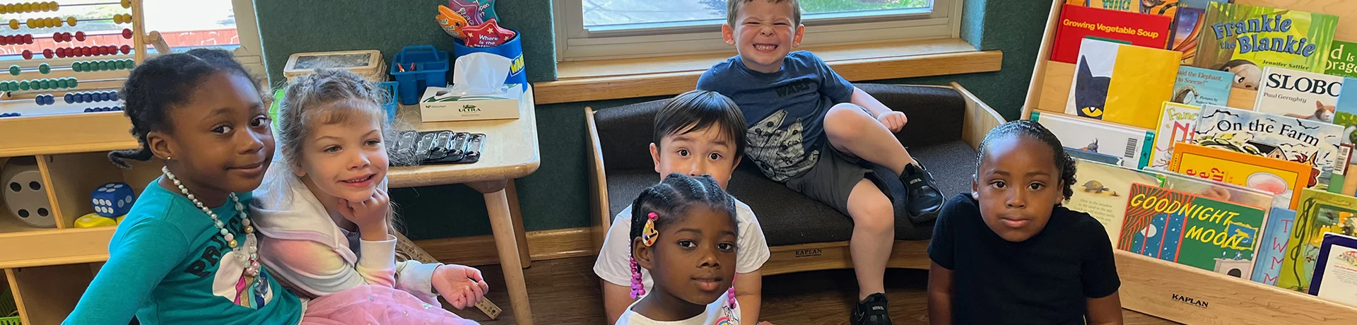 Childcare Day Care Programs - Group of children surrounded by books and educational toys smiling at camera Childcare Programs: More Than Daycare
